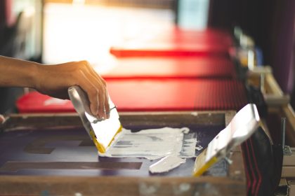Red t-shirt screen printing, worker working on manual screen pri